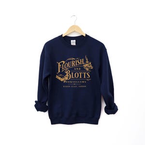 May include: A navy blue sweatshirt with the text "Flourish and Blotts Booksellers Diagon Alley, London" in gold lettering. The text is in a vintage style font and is surrounded by a decorative border.