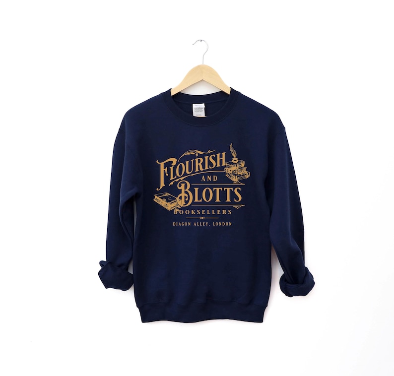 May include: A navy blue sweatshirt with the text "Flourish and Blotts Booksellers Diagon Alley, London" in gold lettering. The text is in a vintage style font and is surrounded by a decorative border.