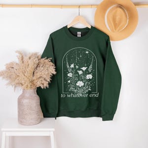 May include: A dark green sweatshirt with a white floral design and the text "to whatever end".