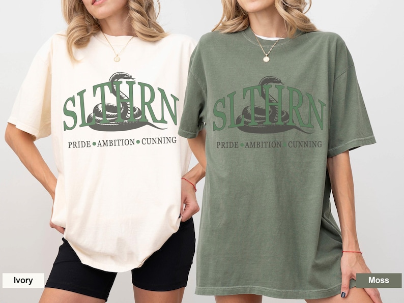 May include: Two t-shirts with a green snake graphic and the text "SLYTHERN PRIDE AMBITION CUNNING". The shirt on the left is ivory and the shirt on the right is moss.
