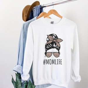 May include: White sweatshirt with a black and white illustration of a woman with a messy bun and sunglasses. The bun has a leopard print headband. The text "#MOMLIFE" is printed below the illustration.