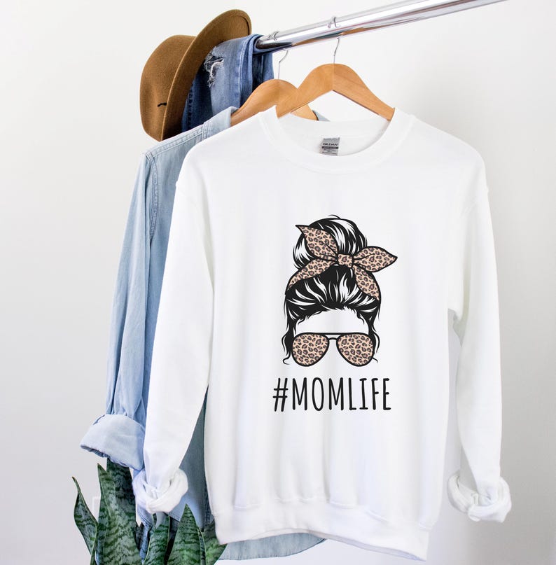 May include: White sweatshirt with a black and white illustration of a woman with a messy bun and sunglasses. The bun has a leopard print headband. The text "#MOMLIFE" is printed below the illustration.