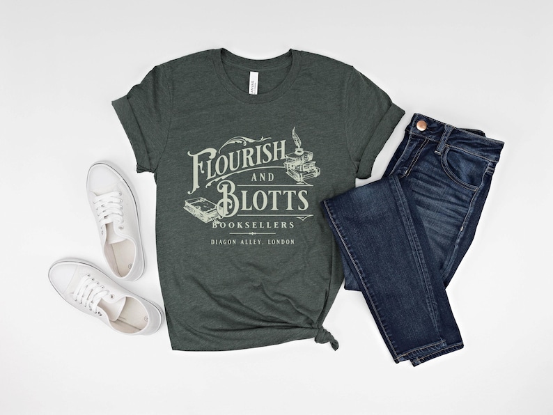 May include: A dark green t-shirt with the text "Flourish and Blotts Booksellers Diagon Alley, London" in white. The shirt is folded and laid out on a white surface with a pair of white sneakers and a pair of blue jeans.