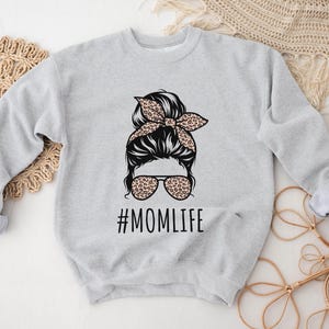 May include: A gray sweatshirt with a graphic of a woman with a messy bun and sunglasses. The text "#MOMLIFE" is printed below the graphic.