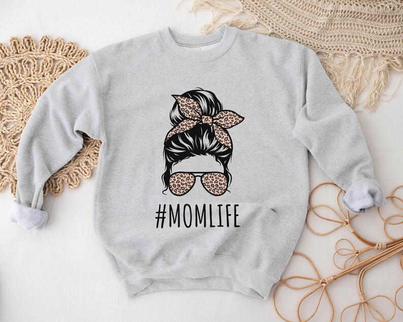 May include: A gray sweatshirt with a graphic of a woman with a messy bun and sunglasses. The text "#MOMLIFE" is printed below the graphic.