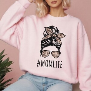 May include: Pink sweatshirt with a graphic of a woman with a messy bun, sunglasses, and a leopard print headband. The text "#MOMLIFE" is printed below the graphic.