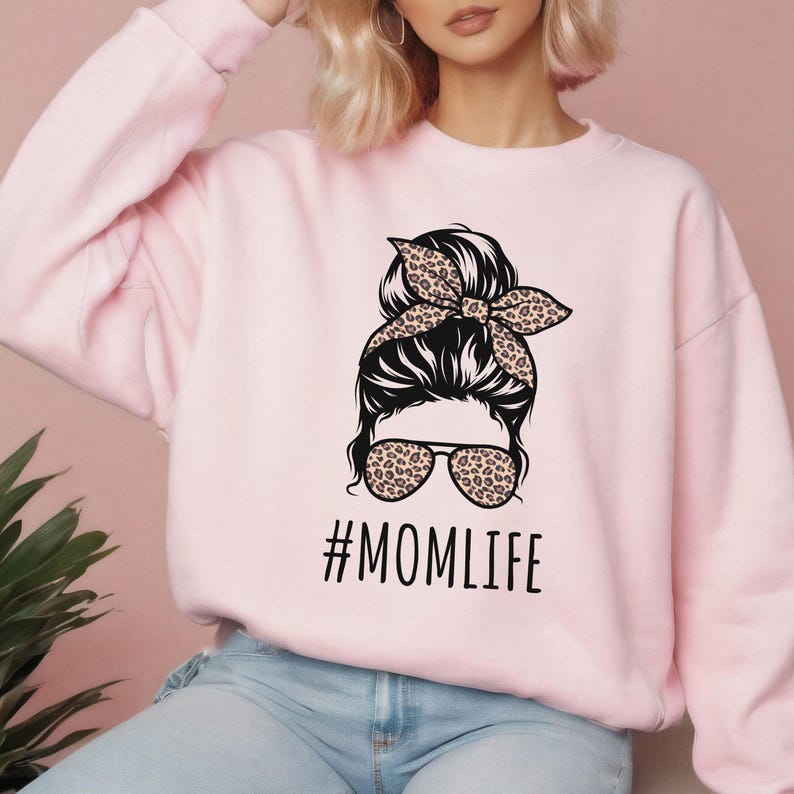 May include: Pink sweatshirt with a graphic of a woman with a messy bun, sunglasses, and a leopard print headband. The text "#MOMLIFE" is printed below the graphic.