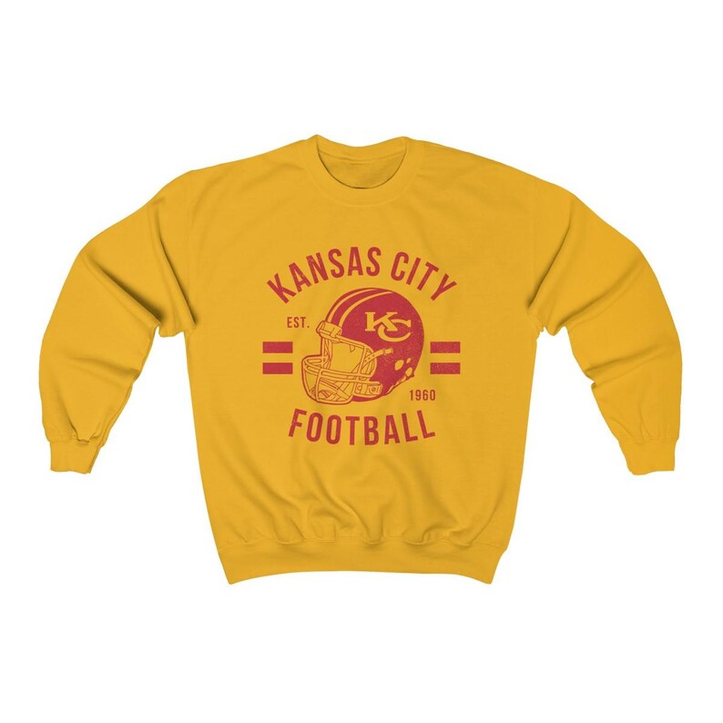 Pode incluir: Uma camisa de moletom amarela com um logotipo vermelho e branco do Kansas City Football. O logotipo apresenta um capacete de futebol com as letras "KC" dentro. O texto "Kansas City" est&aacute; acima do capacete e "Football" est&aacute; abaixo. O texto "Est. 1960" est&aacute; &agrave; direita do capacete.