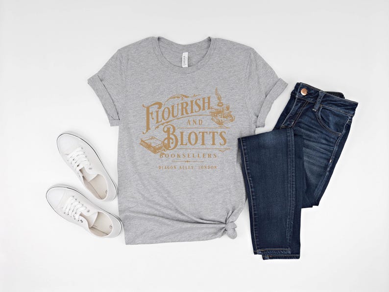 May include: A gray t-shirt with the text "Flourish and Blotts Booksellers Diagon Alley, London" in gold lettering. The shirt is paired with blue jeans and white sneakers.