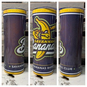 Puede incluir: Un vaso de acero inoxidable con un fondo azul marino y el logotipo amarillo y verde del equipo de b&eacute;isbol Savannah Bananas. El vaso tiene un borde amarillo y las palabras "Savannah Bananas Baseball Club" est&aacute;n impresas en la parte inferior.