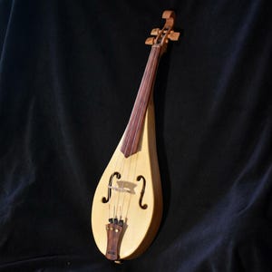 Puede incluir: Un instrumento musical de cuerda con forma de lágrima, cuerpo de madera clara, diapasón de madera oscura y puente. Presenta dos aberturas acústicas en forma de f, cuatro cuerdas metálicas y un cordal de madera oscura con clavijas doradas.