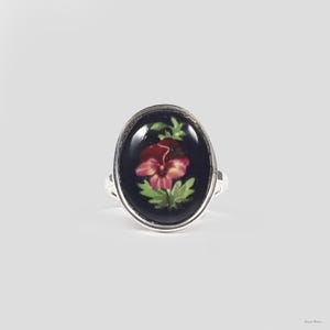 May include: A silver ring with a dark blue oval cameo featuring a pink and white pansy flower with green leaves.