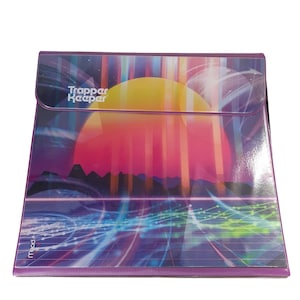 May include: A purple Trapper Keeper binder with a retro sunset design. The cover features a vibrant gradient of colors, including yellow, pink, and blue, with the text "Trapper Keeper" in white. The binder has a snap closure.
