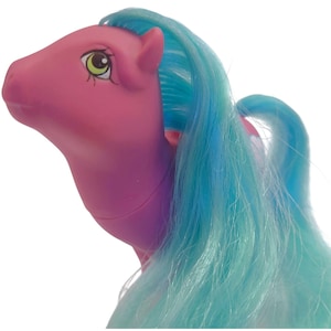 May include: A pink plastic toy pony figure featuring long, flowing light blue synthetic hair. The pony has a smooth, matte finish on its body, large almond-shaped eyes with green irises, and a sculpted mane that cascades down its neck.