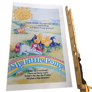 May include: A vintage My Little Pony advertisement featuring a smiling sun, ponies, and a rainbow. The text reads "Look inside for special offers including a FREE Pony poster!" and "Wake up everybody! Open up those eyes! Today's the day the Ponies All plan a big surprise!"