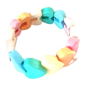 Könnte beinhalten: Ein kreisförmiges Armband, das aus mehreren herzförmigen Perlen in verschiedenen Pastellfarben besteht, darunter Hellblau, Türkis, Gelb, Orange, Rosa und Weiß. Die Perlen sind in einer durchgehenden Schleife aufgereiht und bilden ein lebendiges Accessoire.