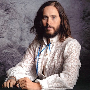 May include: A white lace shirt with a high ruffled collar and long sleeves. The shirt has blue ribbon accents and is buttoned at the front. The person in the image has long brown hair and a beard.