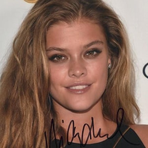 Peut inclure: Portrait d'une personne aux longs cheveux châtain clair et portant un haut noir. La personne sourit légèrement, avec du maquillage visible sur les yeux. L'image comprend une signature à l'encre noire en bas.