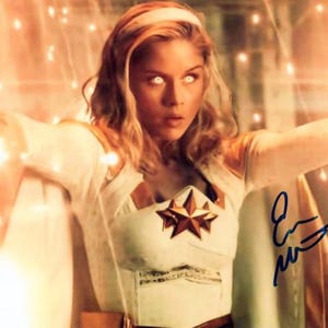 May include: A woman with blonde hair wearing a white costume with a gold star on the chest. She is holding her arms out and glowing light is coming from her hands. The image is signed "E.R."
