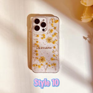 May include: A clear phone case with a pressed flower design and gold glitter. The case has a name "KAYLENA" printed on it.  Style 10.
