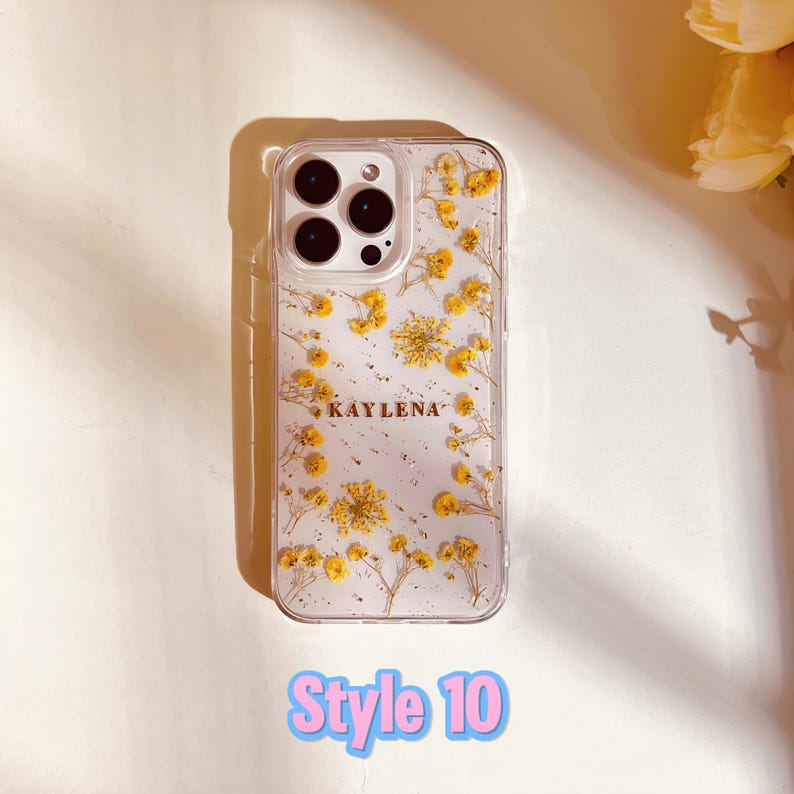 May include: A clear phone case with a pressed flower design and gold glitter. The case has a name "KAYLENA" printed on it.  Style 10.