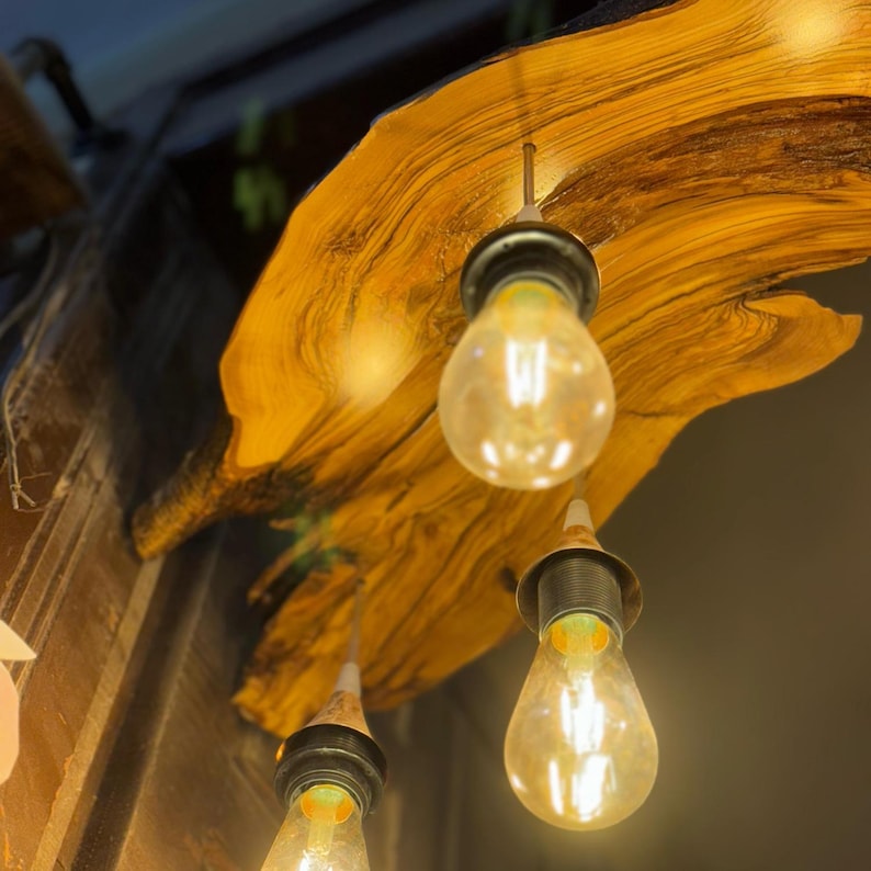 May include: A wooden light fixture with three hanging light bulbs. The wood is a natural, light brown color with dark brown streaks. The light bulbs are clear glass with a warm white glow.