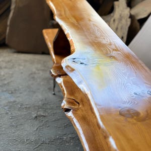 K&ouml;nnte beinhalten: Ein langes, naturbelassenes Holzregal mit einer lebenden Kante und einer nat&uuml;rlichen Oberfl&auml;che. Das Regal hat einen rustikalen Look und wird von Metallbeinen getragen.