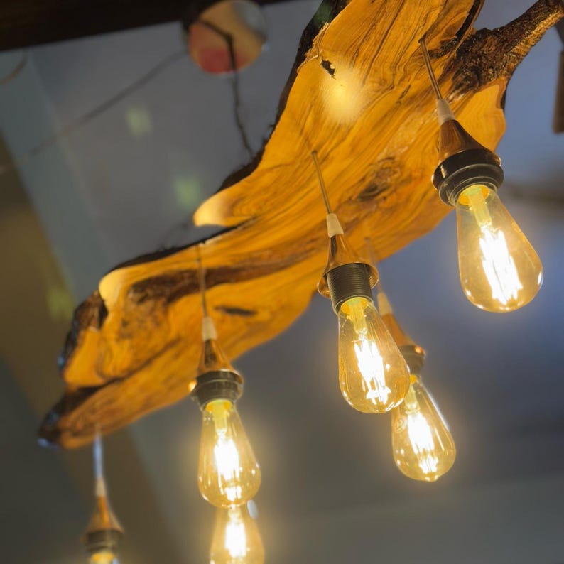 May include: A rustic wooden chandelier with six Edison bulb lights. The wood is a light brown color and has a natural, organic shape. The bulbs are all lit and casting a warm glow.