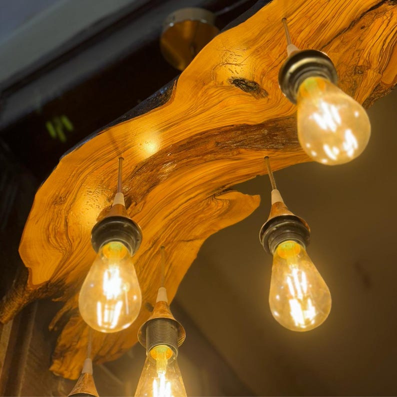 May include: A rustic wooden chandelier with five light bulbs. The wood is a natural, light brown color with dark brown streaks. The light bulbs are clear glass and emit a warm, yellow light.