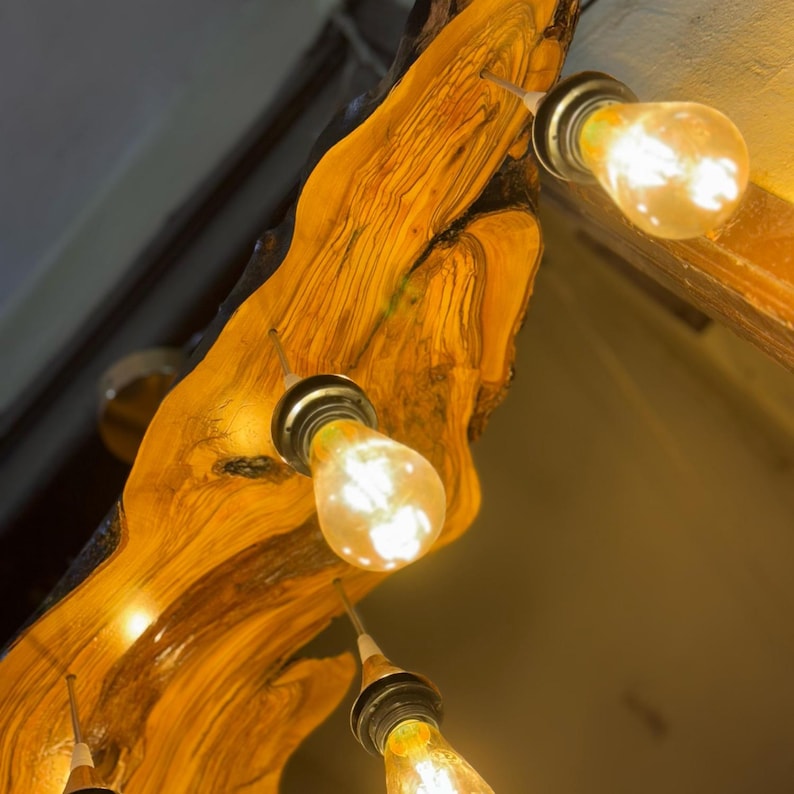May include: A wooden light fixture with four light bulbs. The wood is a natural, light brown color with dark brown streaks. The light bulbs are all turned on and emitting a warm, yellow light.