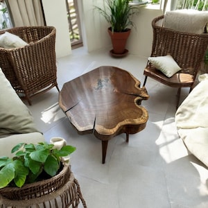 Könnte beinhalten: Ein großer, runder Holz-Couchtisch mit einer natürlichen Holzoptik und einem Live-Edge-Design. Der Tisch hat drei Beine und steht auf einem weißen Fliesenboden.