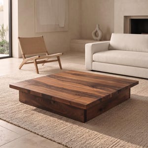May include: A low-profile square coffee table constructed from dark brown wood with a visible natural grain pattern. The table features a thick, flat top surface supported by a recessed base, creating a solid, block-like appearance.