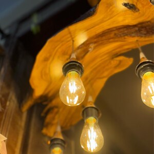 May include: A wooden ceiling fixture with four light bulbs. The fixture is made of a natural wood with a rustic finish. The light bulbs are clear glass and emit a warm, yellow light.