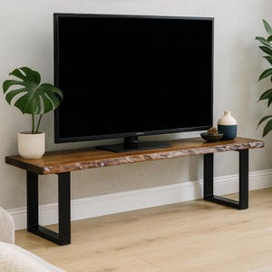 May include: A wooden TV stand with a live edge top and black metal legs. The stand is supporting a large black flat-screen television. A potted plant and decorative items are on the stand. The stand is approximately 72 inches long.