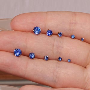Op de afbeelding: Een verzameling blauwe edelsteen oorknopjes in verschillende maten. De oorbellen zijn rond en briljant geslepen, met een helder, reflecterend oppervlak. De oorbellen worden op een lichte achtergrond gepresenteerd.