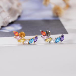Puede incluir: Dos pendientes de botón curvos con una hilera de piedras preciosas de talla marquesa en un degradado de colores naranja, rosa, amarillo, transparente, azul y morado. Uno tiene un poste de metal dorado y el otro un poste de metal plateado.
