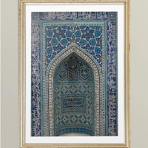 Peut inclure: Impression encadrée présentant un gros plan détaillé d'un mur carrelé orné, bleu et blanc, avec calligraphie arabe. Le motif comprend des motifs géométriques et une niche centrale arquée, dans un cadre doré.