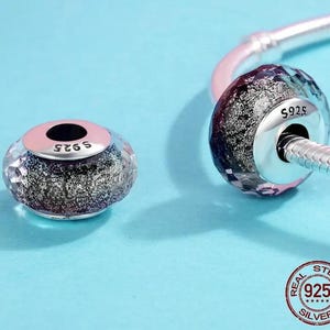 May include: Two sterling silver charm beads with faceted, clear and dark purple glass. One bead is on a silver bracelet. The beads have a pink band and the text "S925". The image has a "Real Sterling Silver" seal.