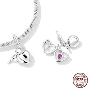 May include: Two sterling silver heart-shaped charm pendants. One is a padlock with a key, the other opens to reveal a pink gemstone. The charms are attached to a silver bracelet. The image also includes a "925 Sterling Silver" seal.