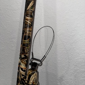 May include: A camouflage-patterned shotgun with a black sling attached to the barrel.