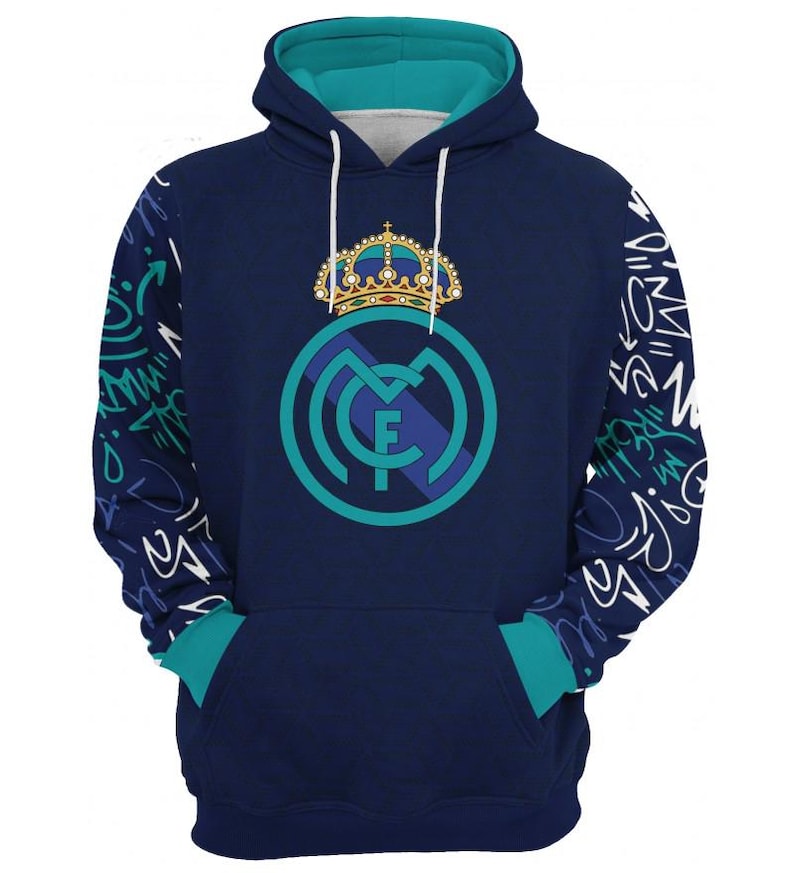 Op de afbeelding: Een marineblauwe hoodie met een teal groene capuchon en bies. De hoodie heeft een witte afbeelding van het Real Madrid-wapen met een kroon erop. De mouwen hebben een wit grafisch patroon.