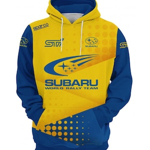 Puede incluir: Una sudadera amarilla y azul con el logotipo del equipo Subaru World Rally. La sudadera tiene un gran logotipo de Subaru en la parte delantera con las palabras "Subaru World Rally Team" debajo. La sudadera también tiene un logotipo de Subaru más pequeño en la manga derecha y la palabra "STI" en la manga izquierda.