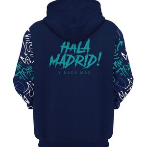 Op de afbeelding: Een marineblauwe hoodie met een witte en groene grafische print op de rug die "Hala Madrid! Y nada mas." zegt.