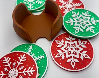 May include: A set of Christmas-themed coasters with a brown holder. The coasters are red and green with white snowflake designs. The holder is a solid brown color and is designed to hold the coasters.