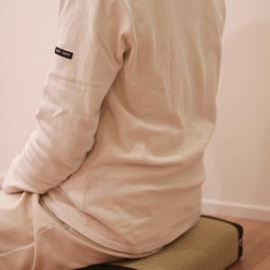 A model is seated on the Agura Tatami Cushion, captured from a rear diagonal angle. With its simple and calming design, the cushion blends seamlessly into the interior space. Its thickness and balanced firmness help stabilize the model’s posture and provide firm support to the pelvis.