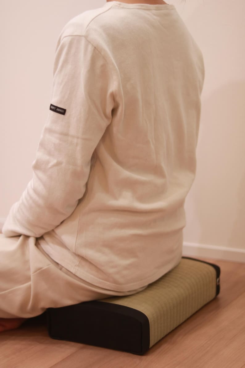 A model is seated on the Agura Tatami Cushion, captured from a rear diagonal angle. With its simple and calming design, the cushion blends seamlessly into the interior space. Its thickness and balanced firmness help stabilize the model’s posture and provide firm support to the pelvis.