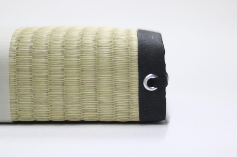 Close-up view of the surface of the Agura tatami cushion. The fine weave of natural rush grass (igusa) from Kumamoto and the contrasting black fabric edging highlight the craftsmanship and refined simplicity of traditional Japanese design.