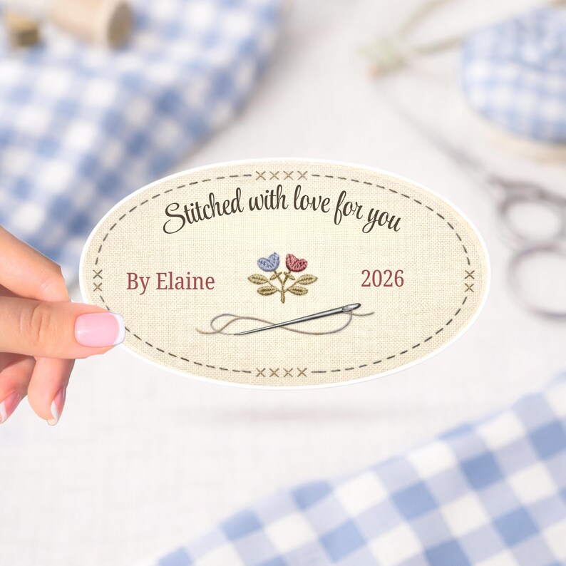 Puede incluir: Una pegatina ovalada con el texto "Stitched with love for you" y "By Elaine 2026". La pegatina presenta un dise&ntilde;o de bordado floral con una aguja e hilo. La pegatina es beige con un borde punteado.