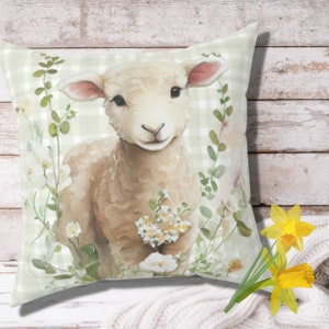 May include: A white lamb with brown spots stands in a field of green and white flowers. The lamb is looking at the camera with a sweet expression. The background is a green and white gingham pattern.