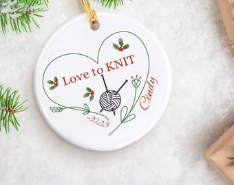May include: White ceramic Christmas ornament with a green heart design. The heart has the text "Love to KNIT" and a drawing of knitting needles and yarn. The ornament also has the text "Cindy" and "2023".